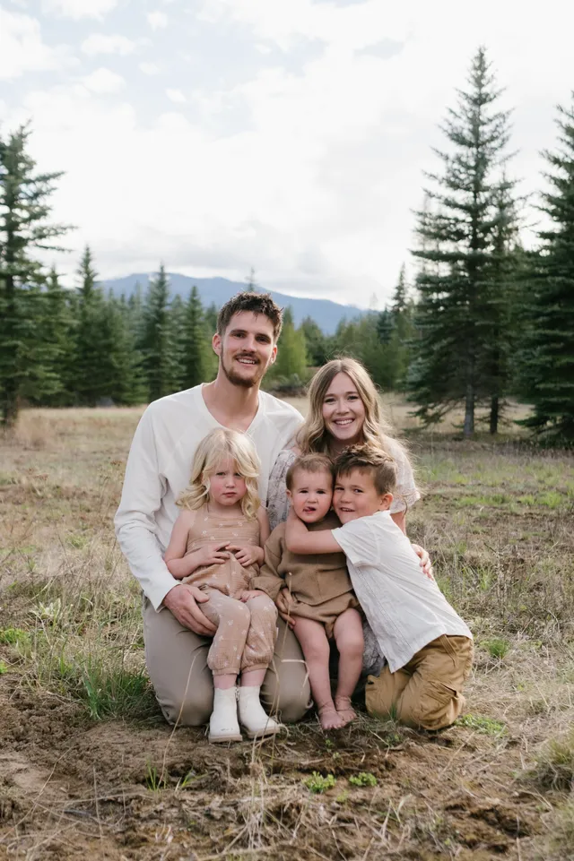Judah and Belle sitting in the grass with their three children, pine trees behind them